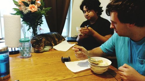 Man with brother having food while looking at cat on table