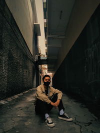 Portrait of young man sitting on alley amidst buildings
