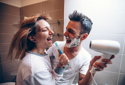 Cheerful man holding dryer for woman in bathroom