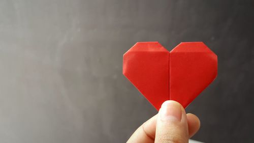 Cropped hand of woman holding paper heart shape against wall