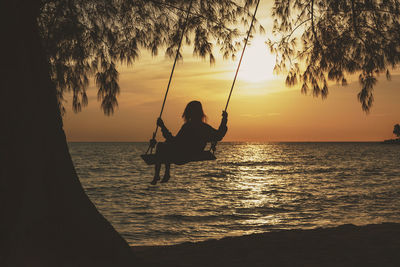 Silhouette woman swinging against sea during sunset