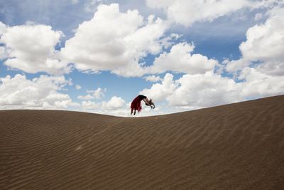 Teenage girls jumping on sand against sky