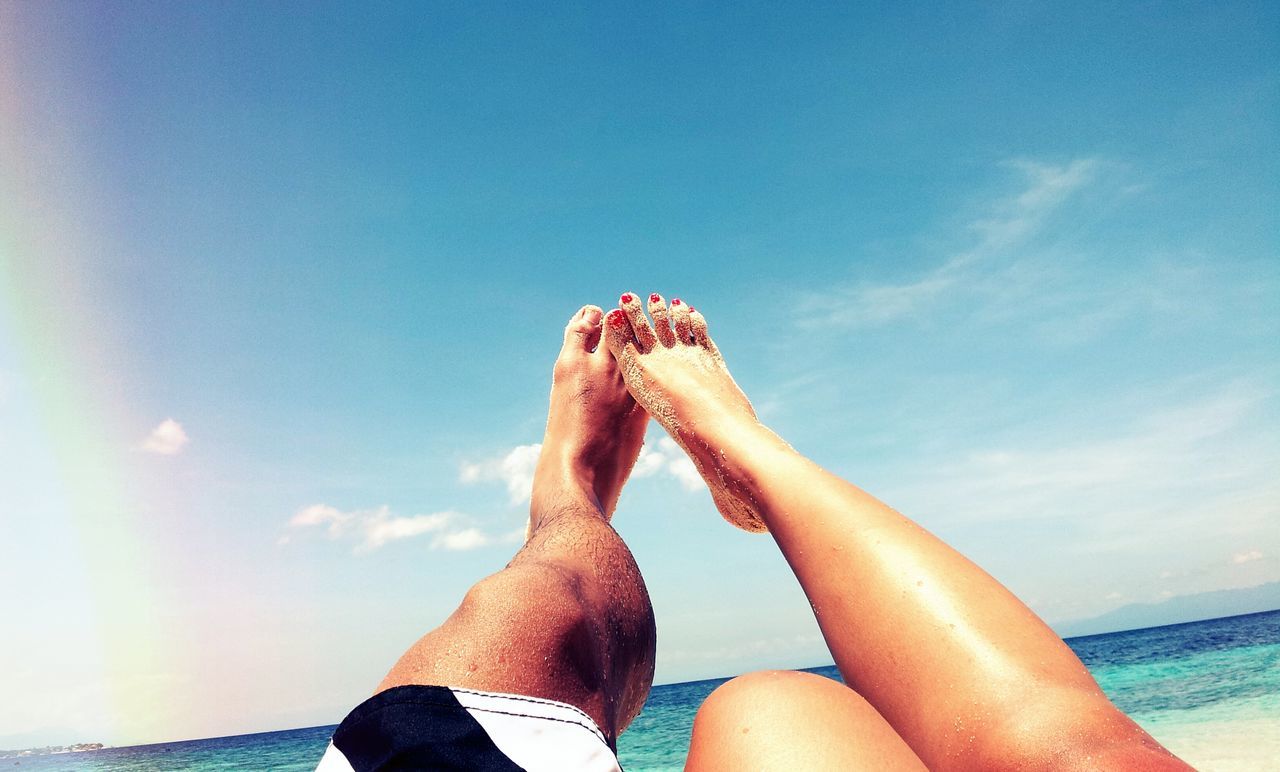 low section, person, lifestyles, sea, barefoot, leisure activity, personal perspective, water, sky, beach, relaxation, blue, horizon over water, sunlight, human foot, sand