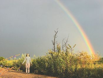 Rear view of man standing on field against rainbow in sky