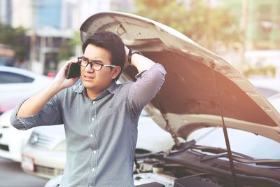 Man talking on phone while standing by broken car