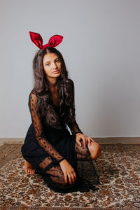 Portrait of beautiful young woman sitting against wall