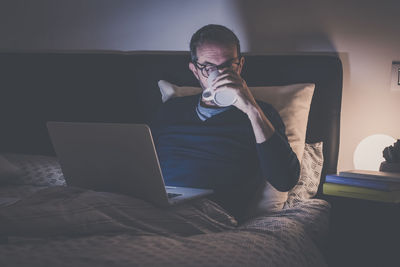 Man works with laptop lying on bed. male home working remote office. boy sit in bedroom use devices