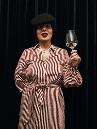 Portrait of woman having wine while standing against wall