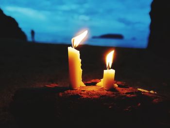 Close-up of burning candles on rock at dusk