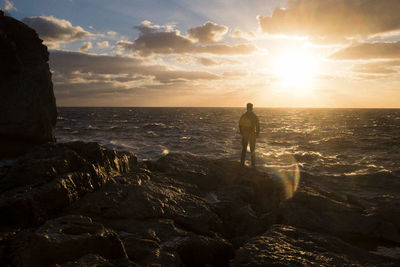 Silhouette man standing on rock at beach against sky during sunset