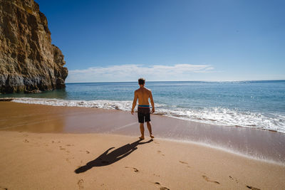 Rear view of shirtless man walking at beach against sky