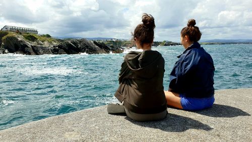 Rear view of women sitting on rock by sea