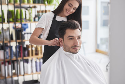 Female hairdresser draping cap to man sitting on chair