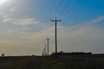 Low angle view of electricity pylon on field against sky during sunset
