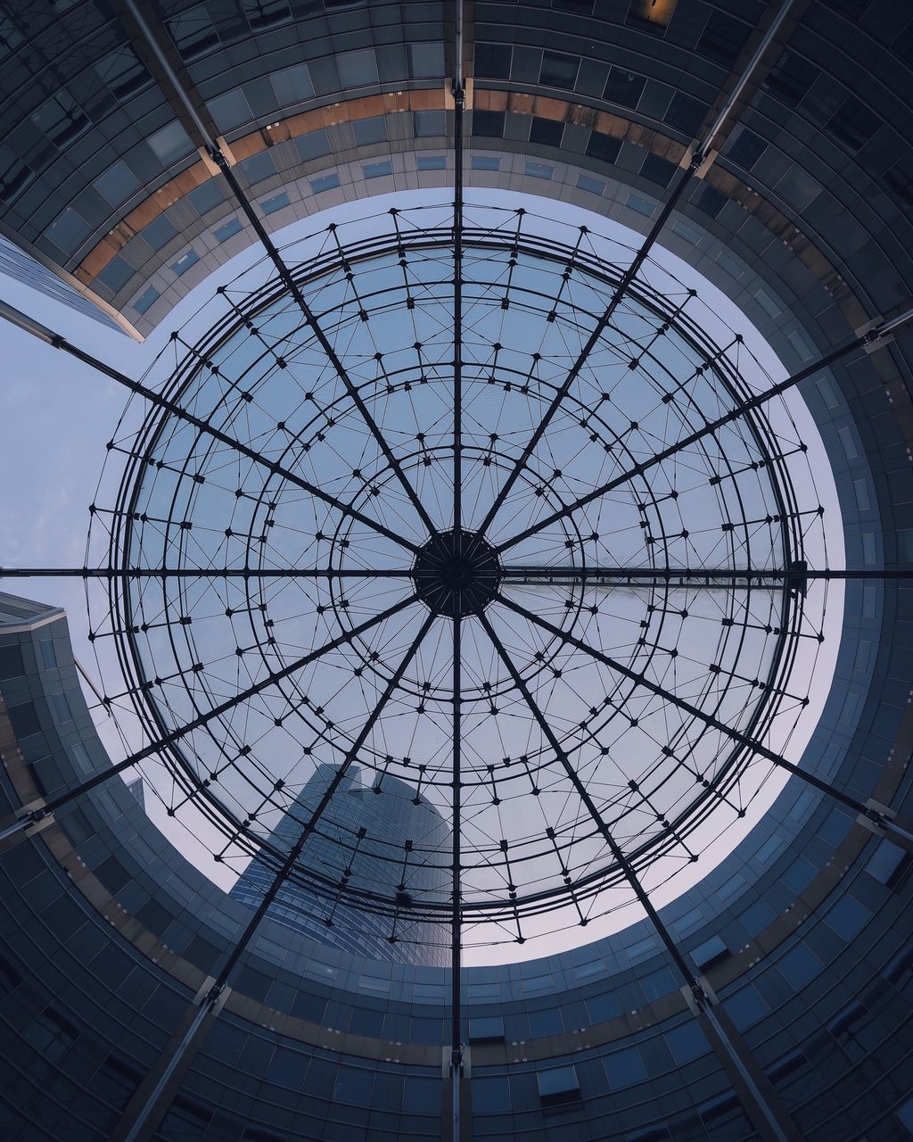 low angle view, built structure, architecture, circle, geometric shape, ceiling, indoors, sky, directly below, pattern, ferris wheel, glass - material, skylight, design, amusement park, no people, day, cloud - sky, backgrounds, building exterior