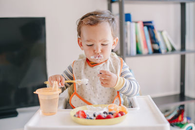Cute caucasian baby boy eating ripe berries and fruits with yogurt. funny smiling child kid eating b