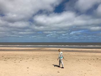 Full length of woman walking on sea shore at beach against cloudy sky