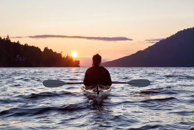 Rear view of silhouette man in sea against sky during sunset