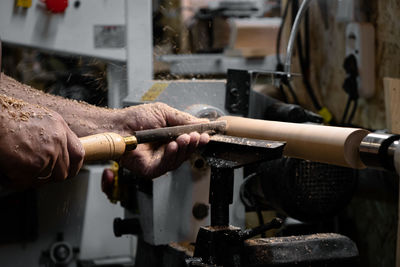 A man in a working apron works on a wood turning lathe. hands hold a chisel. hobby