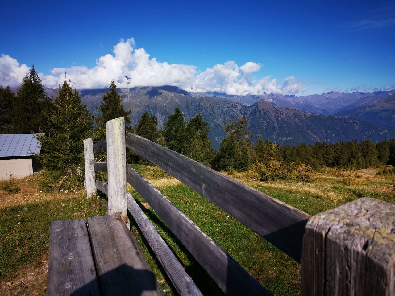 WOODEN BENCH ON FIELD BY MOUNTAIN AGAINST SKY