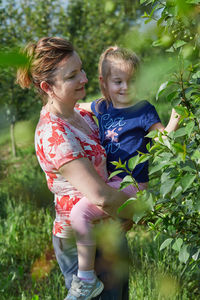 Smiling mother with daughter touching plants at agricultural field