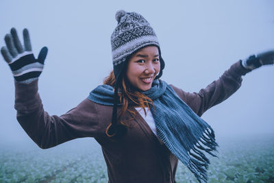 Portrait of cheerful young woman standing at farm during foggy weather