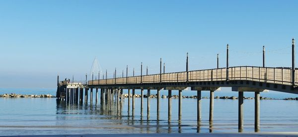 Pier over sea against clear blue sky