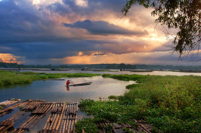 Man sailing in lake against sky during sunset