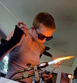 Young woman making glass with flaming torch in factory