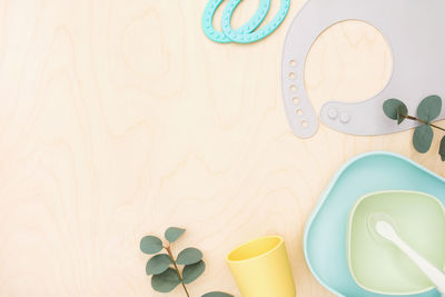 Baby accessories and tableware on wood. first feeding for kids. top view silicone dishware, bib, cup