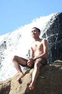 Low angle view of young man sitting on rock