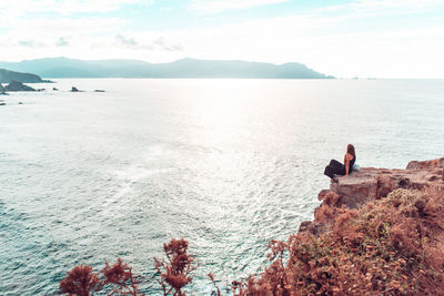 Full length of woman sitting by cliff against sea