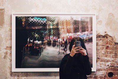 Reflection of man photographing through mobile phone on window