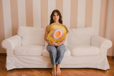 Portrait of woman holding hat sitting on sofa at home