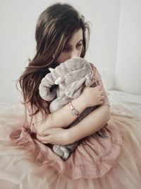 Thoughtful woman with stuffed toy sitting on bed at home