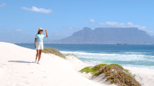 Rear view of woman standing at beach against sky