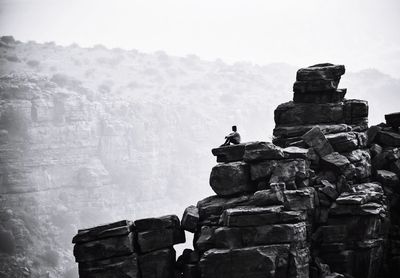 Low angle view of man sitting on rock against sky