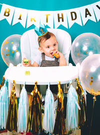 Cute baby boy sitting on high chair in birthday party