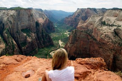 Rear view of woman sitting on rocky mountains