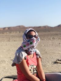 Portrait of woman in sunglasses sitting on land against sky