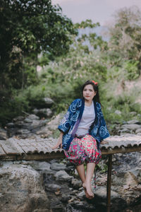 Woman sitting on footbridge over lake against trees in forest