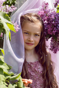 Caucasian girl child seven years old in a purple dress stands in nature with a wreath of lilacs