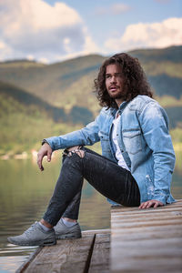 Young man looking away while sitting at lake