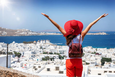 Rear view of woman with arms raised looking at cityscape against sky