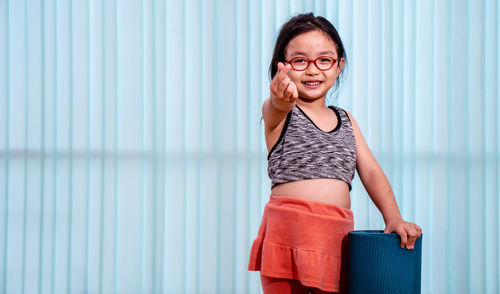 Portrait of smiling young woman standing against wall