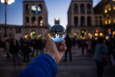 Cropped hand of person holding crystal ball against buildings in city