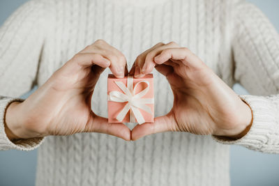 Midsection of woman holding gift box while making heart shape