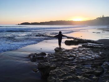 Person standing on rock against sea during sunset