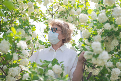 Portrait of young woman standing by flowering plants