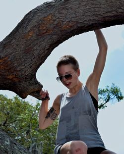 Cheerful woman hanging from branch against clear sky at park